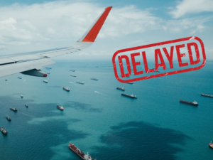 Featured image showing an jet airliner wing flying over several cargo ships