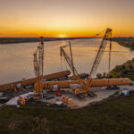 Heavy lift operation at sunset showing oversized LPG storage tank transport along river port