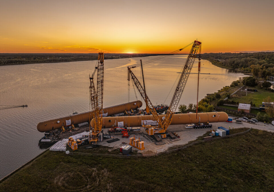 Heavy lift operation at sunset showing oversized LPG storage tank transport along river port